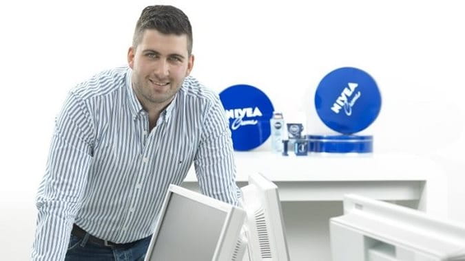 Florian Bock, Informatikkaufmann, lehnt lächelnd auf seinem Schreibtisch